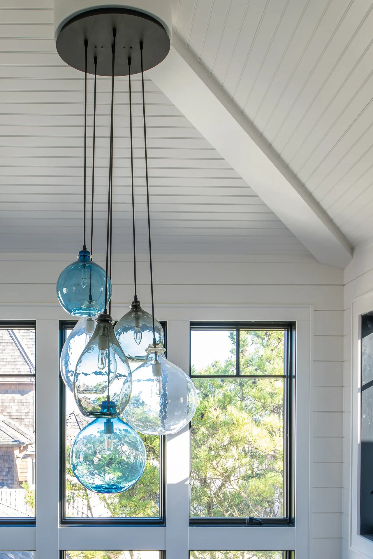 Blue and clear glass pendant lights hang from the ceiling beside large windows in the Porch Talk House.