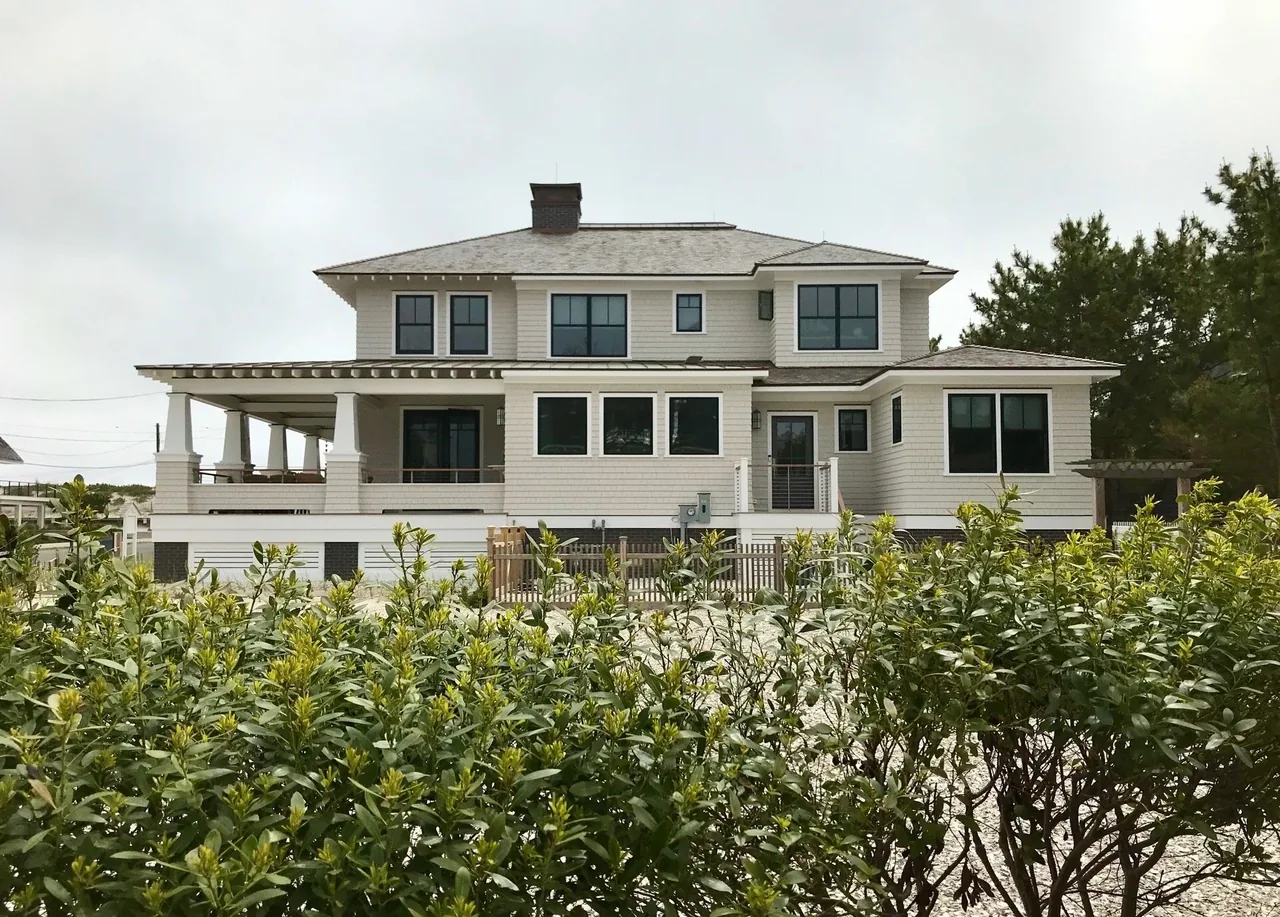 Two-story house featuring shingle siding, black window frames, tapered columns, and a wrap-around porch with porch roof eaves.