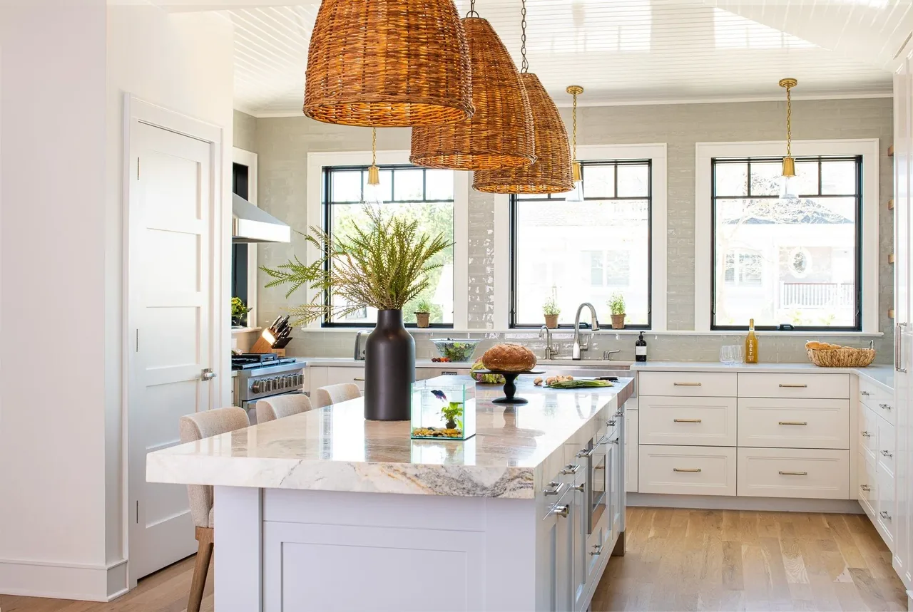 Kitchen features a marble island with seating, three woven pendant lights, and symmetrical black-framed windows.