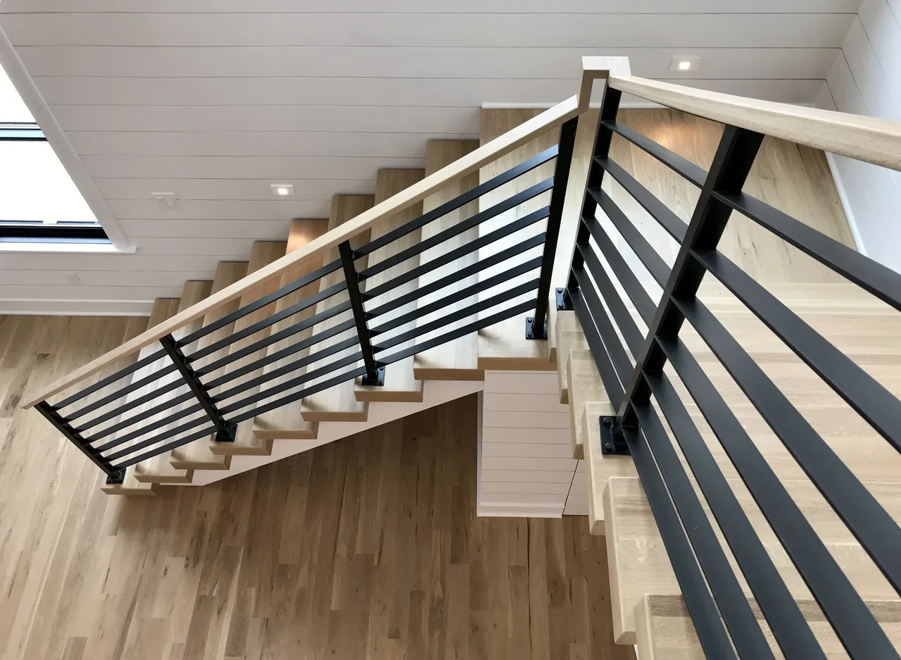 Interior staircase with light wood steps and black horizontal metal cable railing in Porch Talk House, Seaside Park.