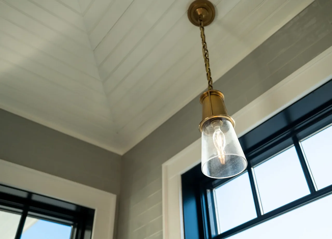 Pendant light with glass shade hangs from a vaulted ceiling with white shiplap near black window frames.