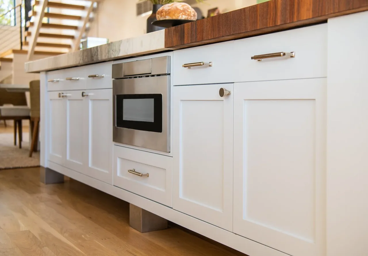 Modern kitchen island with white cabinets, stainless steel microwave, and mixed wood and stone countertop in Porch Talk House.