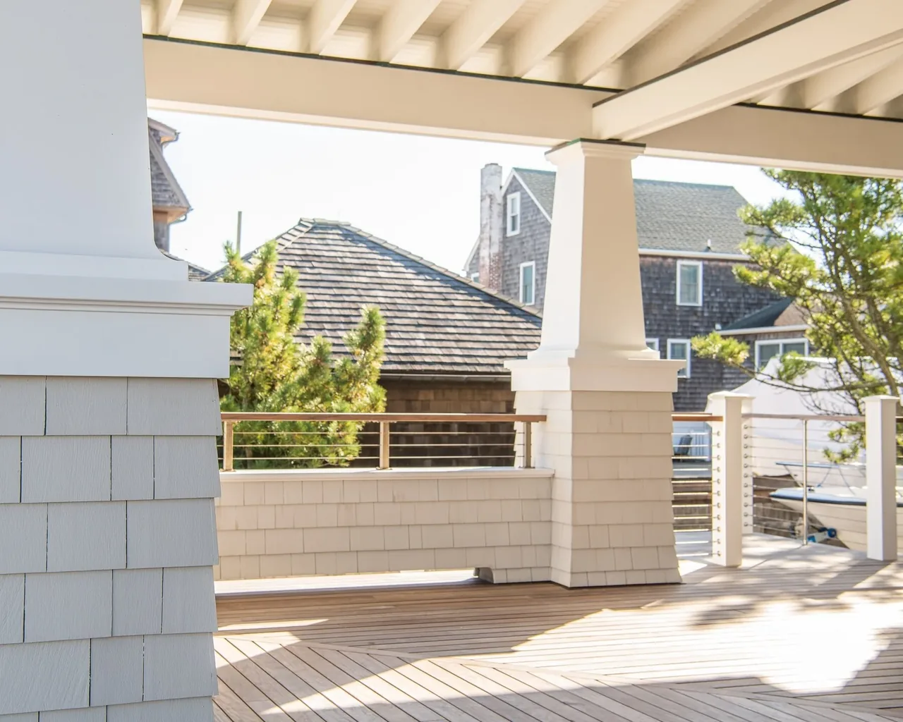 Covered porch featuring tapered columns, shingle siding, horizontal cable railing, and wood decking at Porch Talk House.