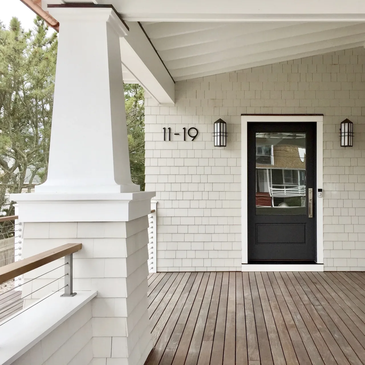 Wrap-around porch with white shingle siding and tapered columns at Porch Talk House by Richard Bubnowski Design.