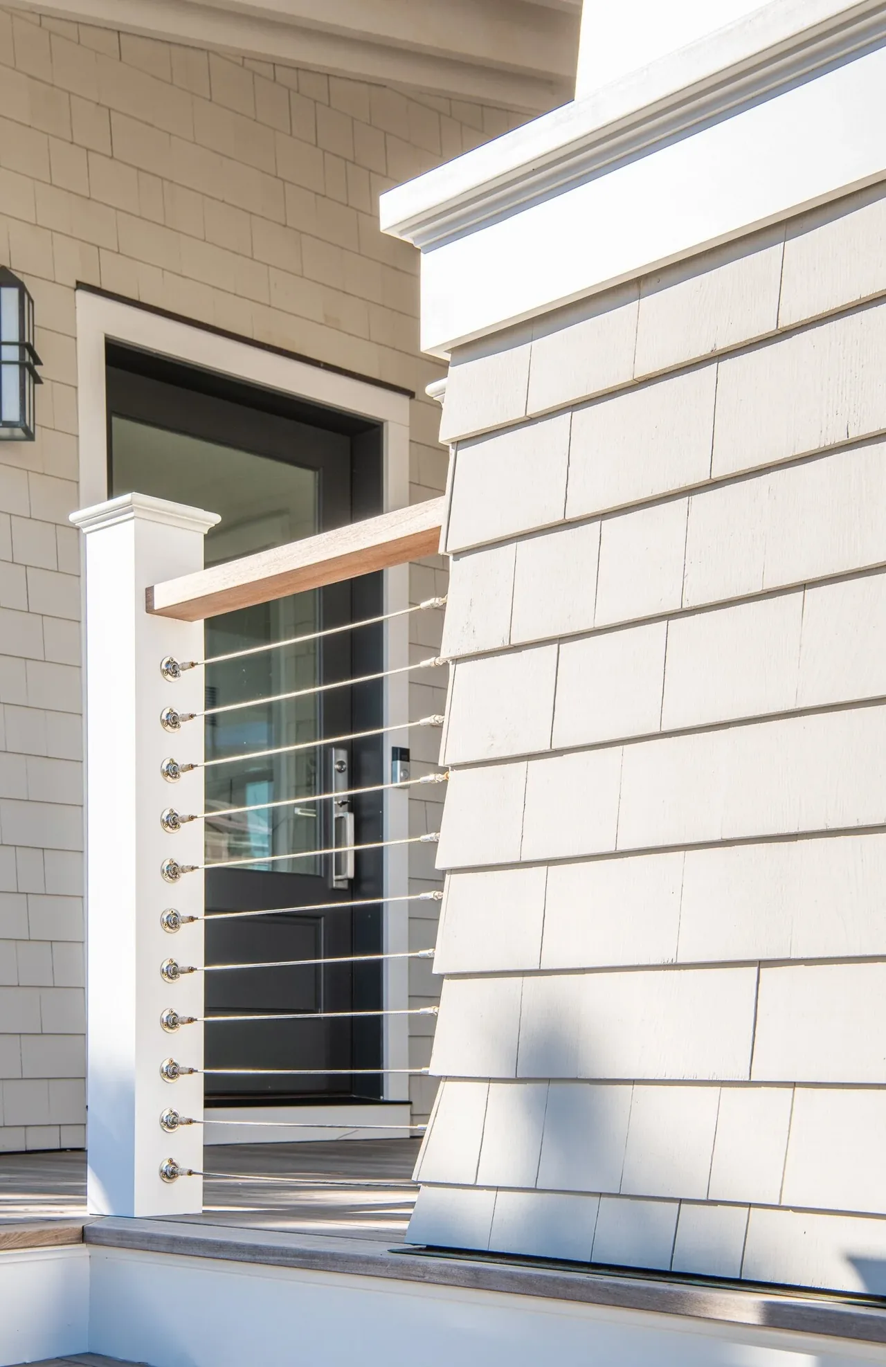 Modern porch railing featuring stainless steel cable infill and white shingle siding at the Porch Talk House.