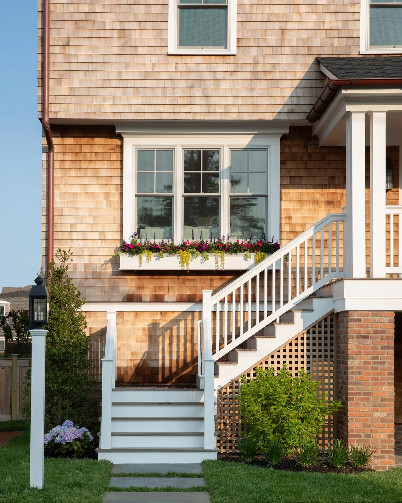 Raised porch and stairs with white railings on a house featuring natural wood shingle siding and a flower box under the window.
