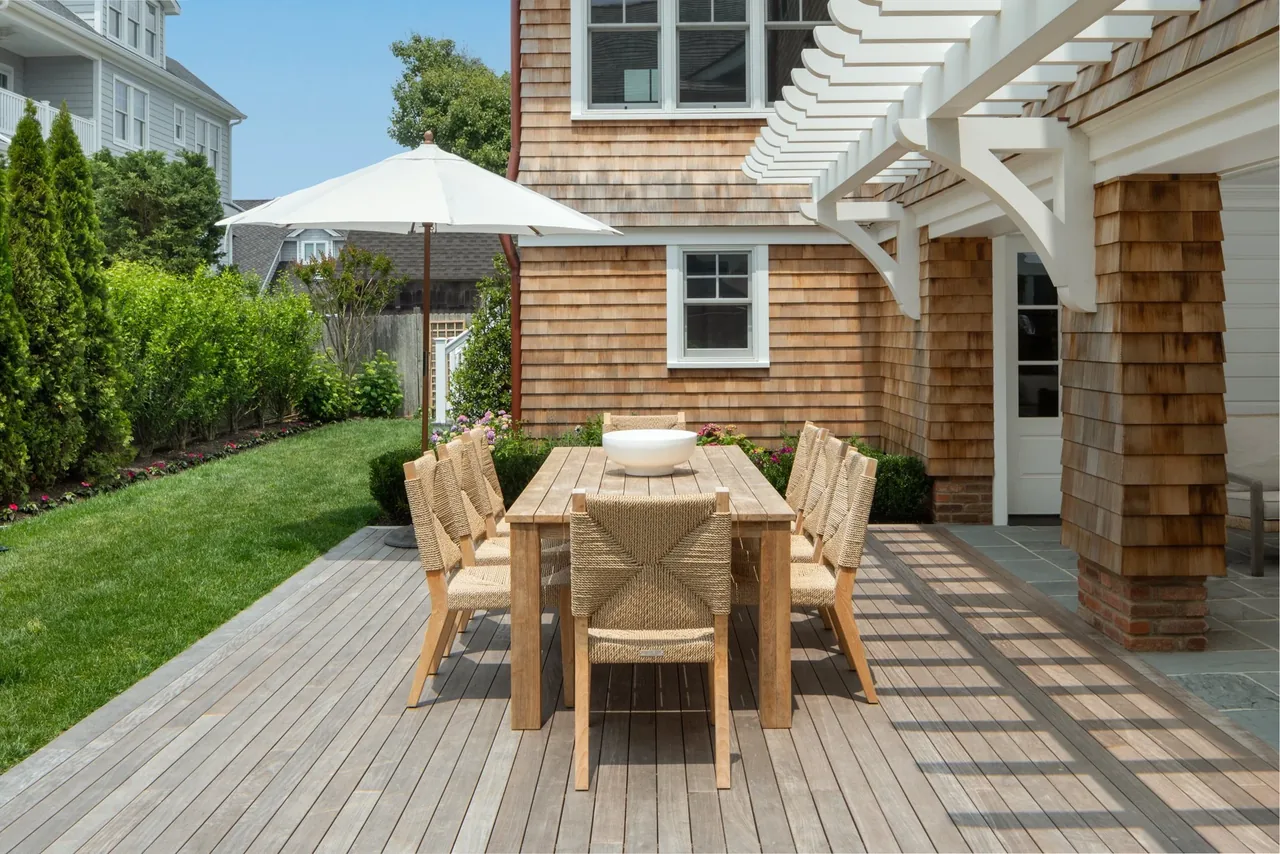 Outdoor dining space on a wood deck adjacent to the shingle-sided Hagerstrom residence with a white pergola above.