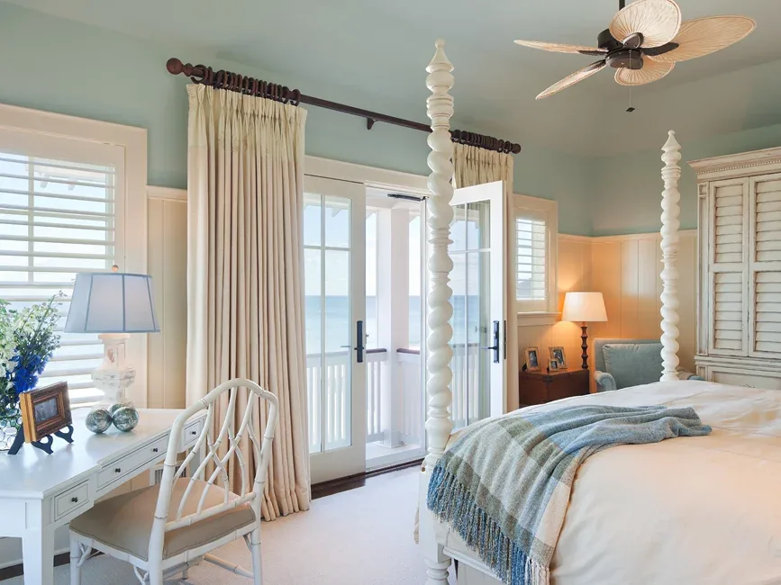 Bedroom featuring a white four-poster bed and glass doors leading to a balcony overlooking the ocean.
