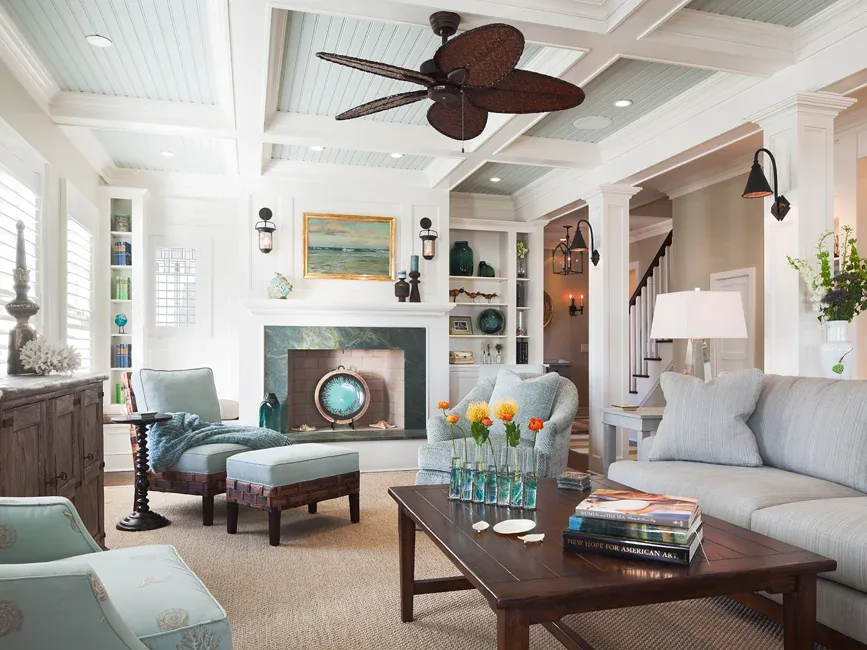 Living room featuring a fireplace with built-in shelving and a ceiling fan with woven blades in a coastal-inspired home.