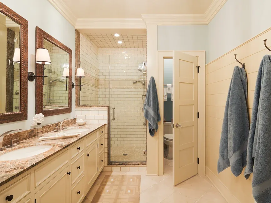 Bathroom with dual sinks and a marble countertop next to a walk-in shower with white subway tile walls.