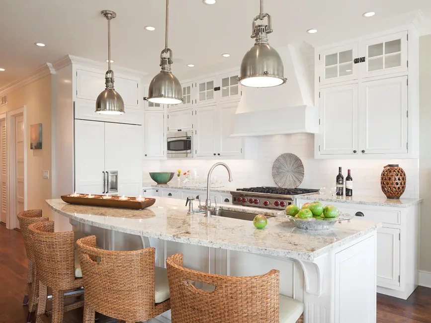 Kitchen with white cabinetry, marble countertops, wicker seating, and stainless steel pendant lighting.