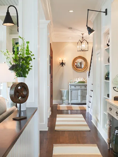 Interior hallway with hardwood flooring, striped rugs, and various light fixtures including sconces and a lantern pendant.