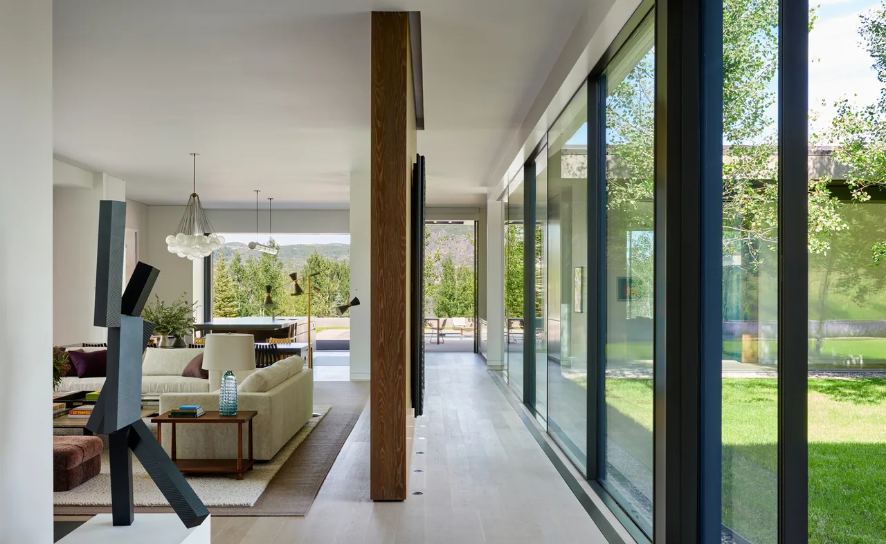 Mountain Modern living area with floor-to-ceiling black window frames and views of grassy lawn and mountains.