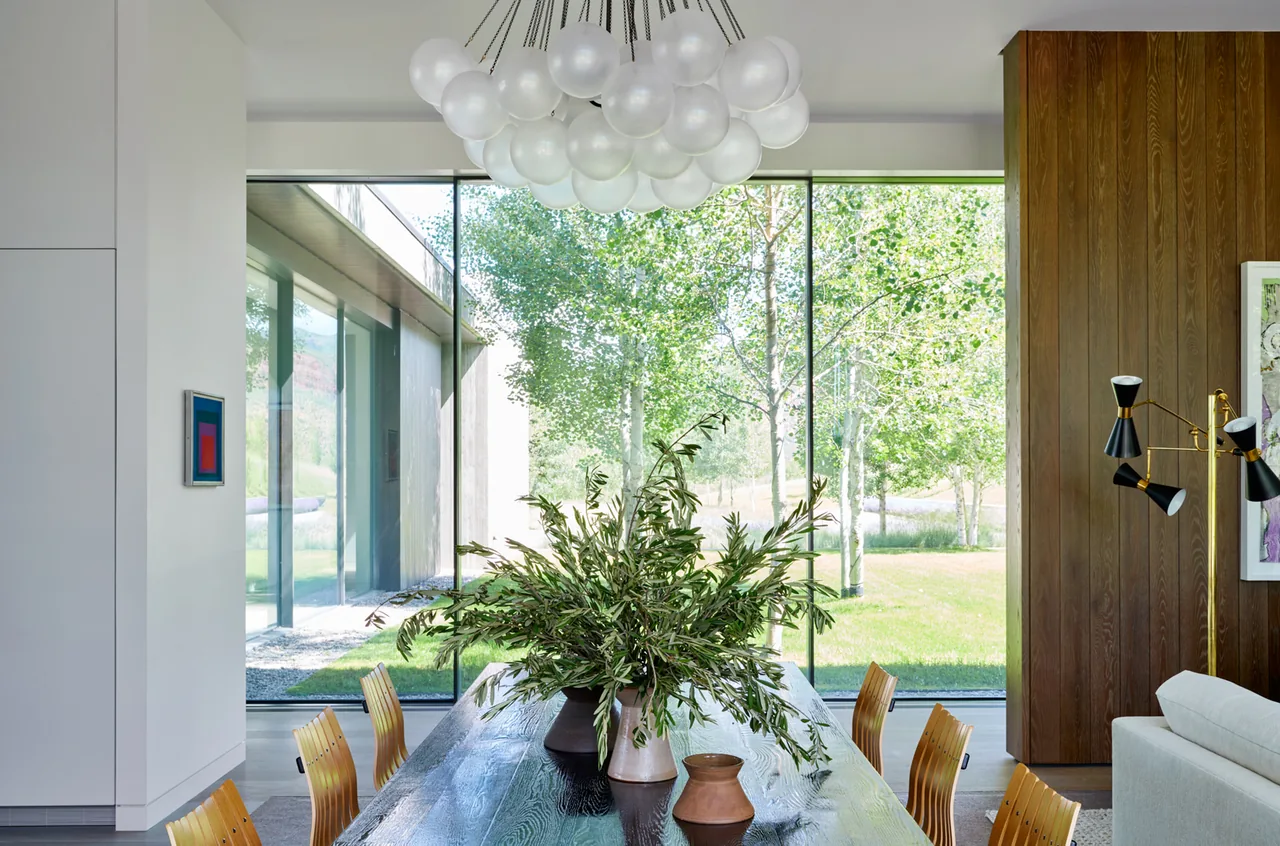 The Mountain Modern dining area features a large wood table, natural light from floor-to-ceiling glazing, and a sculptural pendant light.