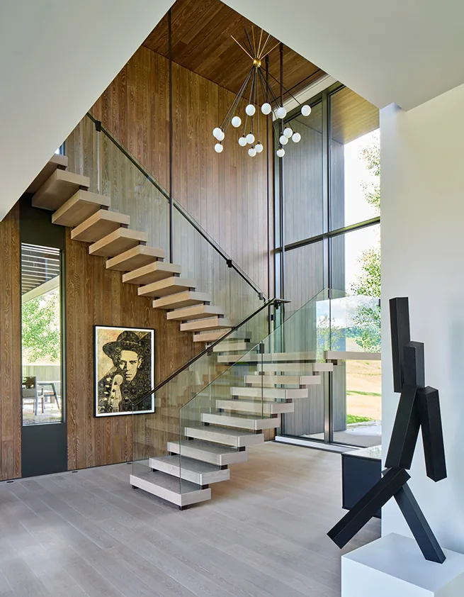 Floating staircase with glass railing and wood panel walls in a modern-style home interior.