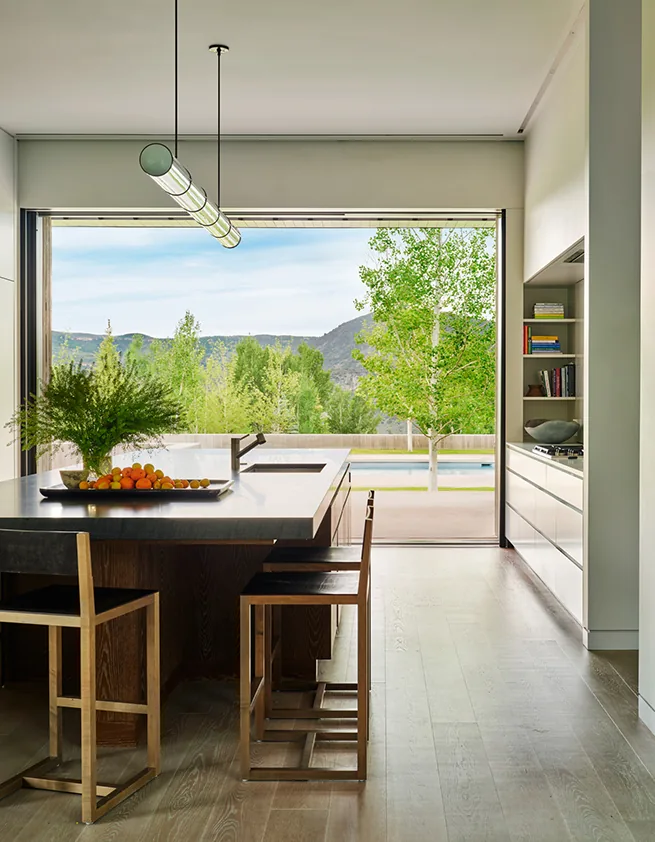 Mountain Modern kitchen features an island with seating and expansive glass wall opening to a pool and mountain landscape.