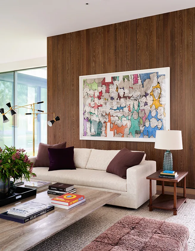 Mountain Modern living room features a wood-paneled wall with colorful abstract art and floor-to-ceiling glazing for landscape views.
