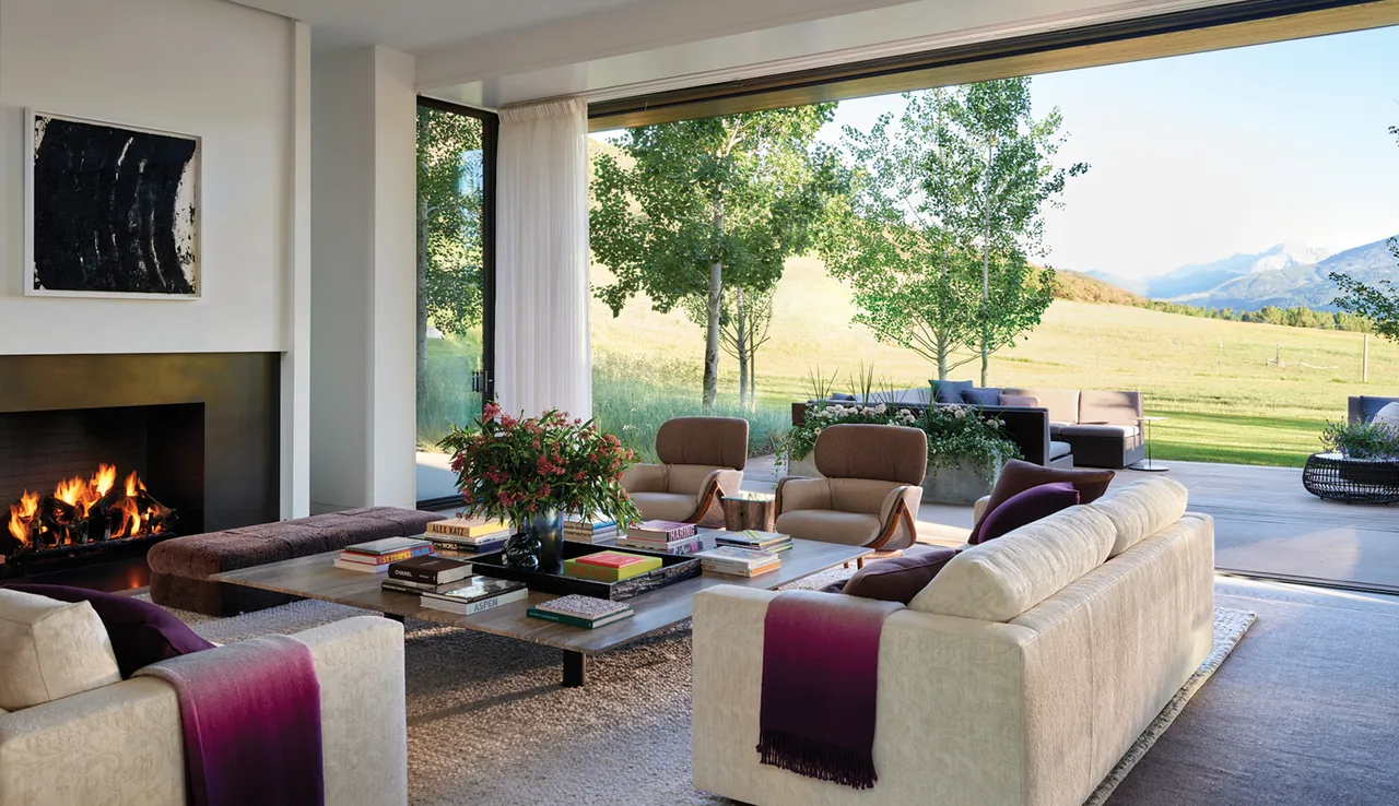Mountain Modern living room with fireplace and large sliding glass doors opening to an outdoor seating area and mountain landscape.