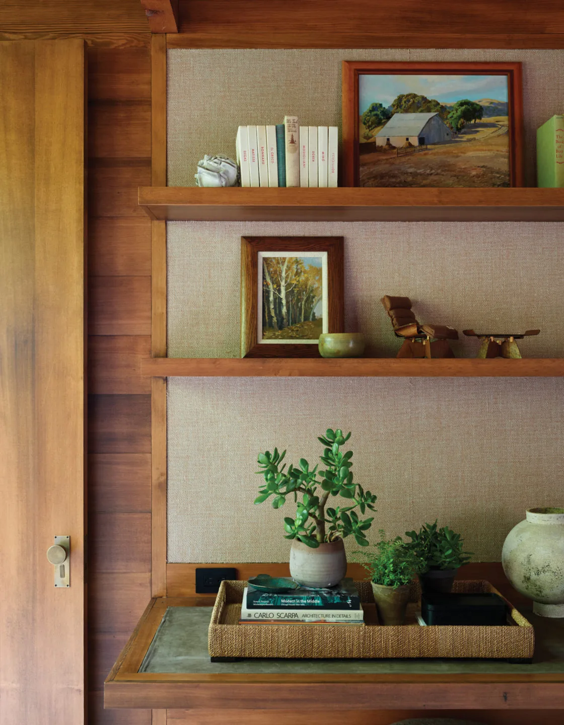 Wood shelving and a desk area with artwork, books, and potted plants highlight wood panel wall details.