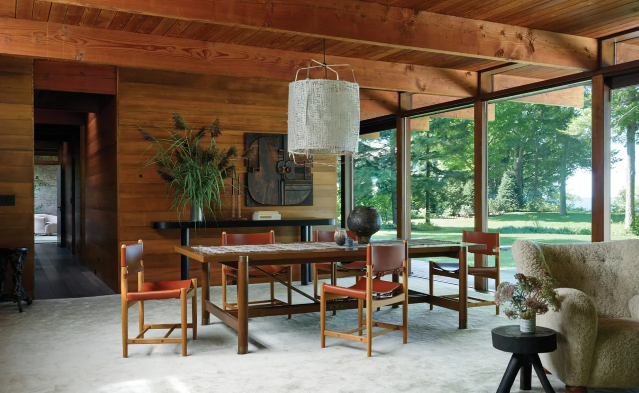 Dining area in a midcentury home featuring wood beams and floor-to-ceiling glazing with views of lush greenery.