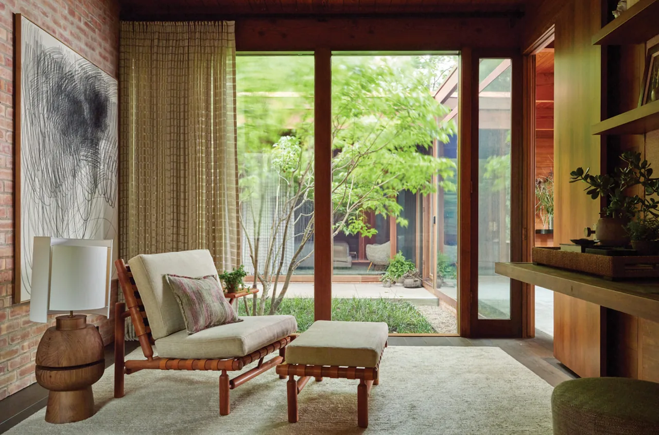 Living room in Lakeside Midcentury project features a wood-framed glass door opening to a courtyard space with greenery.