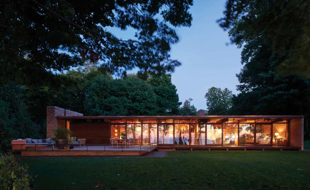 Midcentury modern Lakeside Midcentury house with floor-to-ceiling windows and a flat roof, surrounded by trees and a lawn.