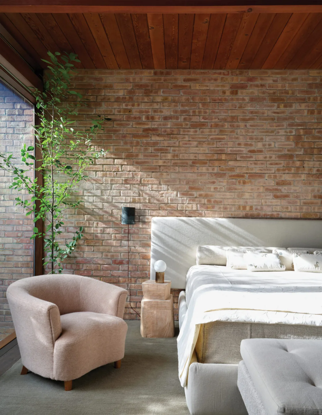 Bedroom featuring a brick wall, wood plank ceiling, and large window illuminating soft furniture.