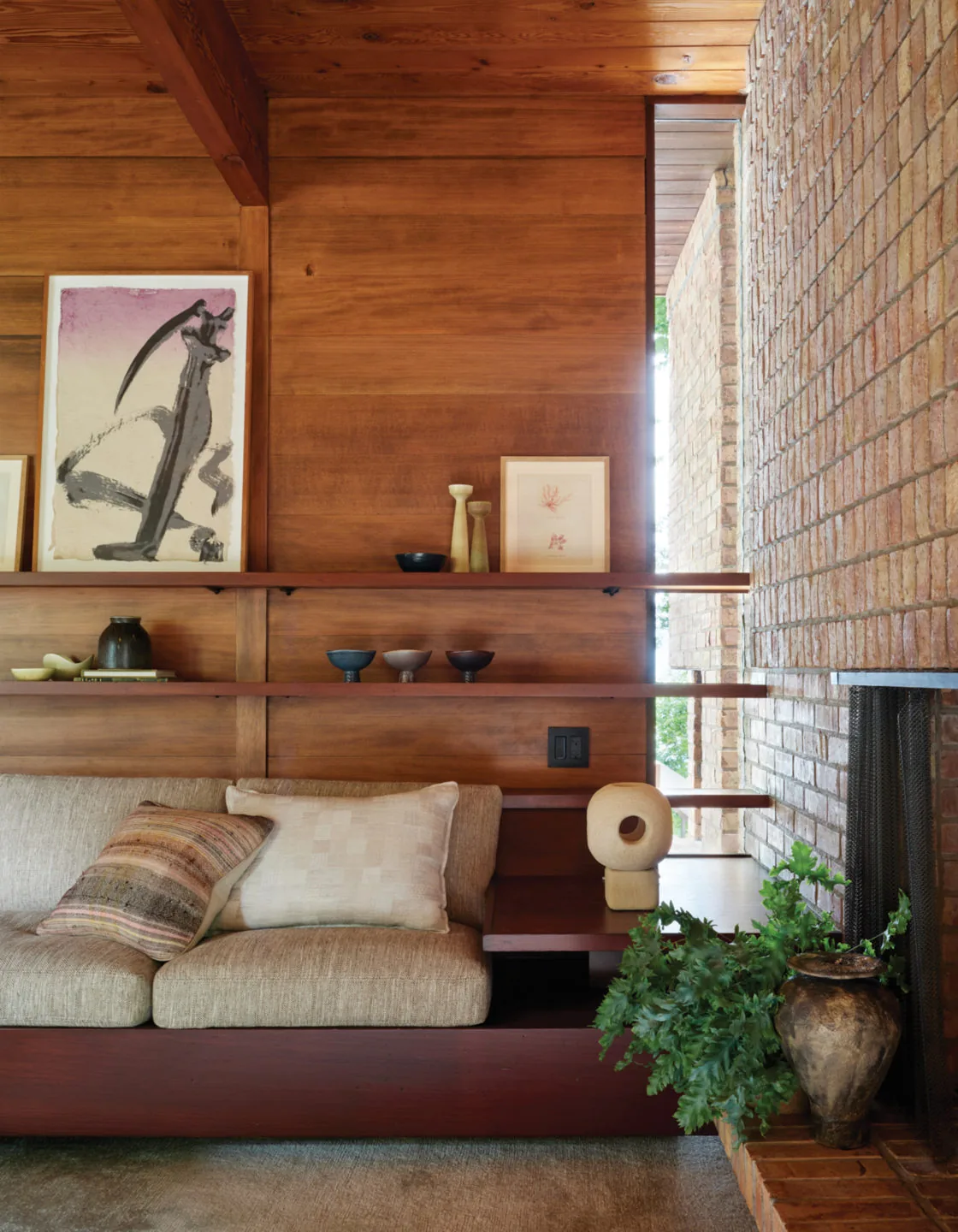 Interior view of a midcentury living room corner featuring a built-in sofa and brick fireplace.