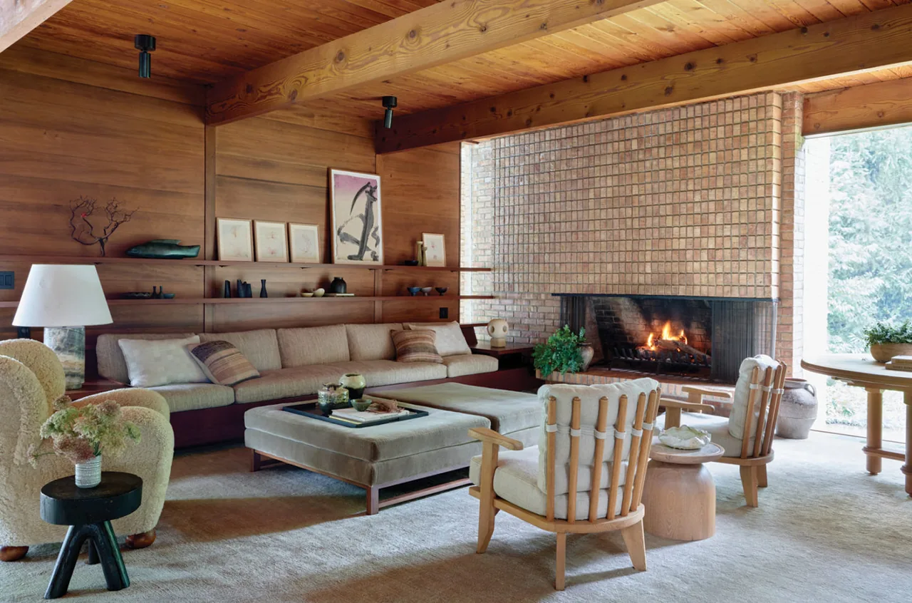 Lakeside Midcentury living room features wood panels, brick fireplace, and a cozy seating arrangement with a beige sectional and soft armchairs.