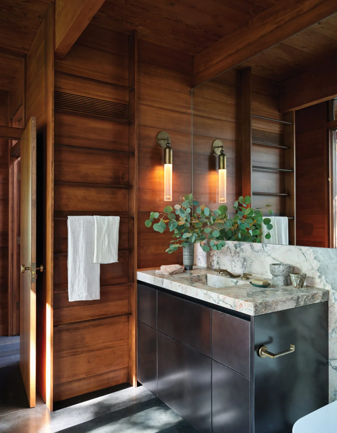 Midcentury-inspired bathroom featuring a marble countertop vanity with bronze fixtures and warm wooden wall paneling.