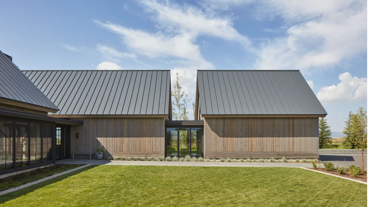 Modern residence features weathered wood siding and a standing seam metal roof with a glass entry hallway.