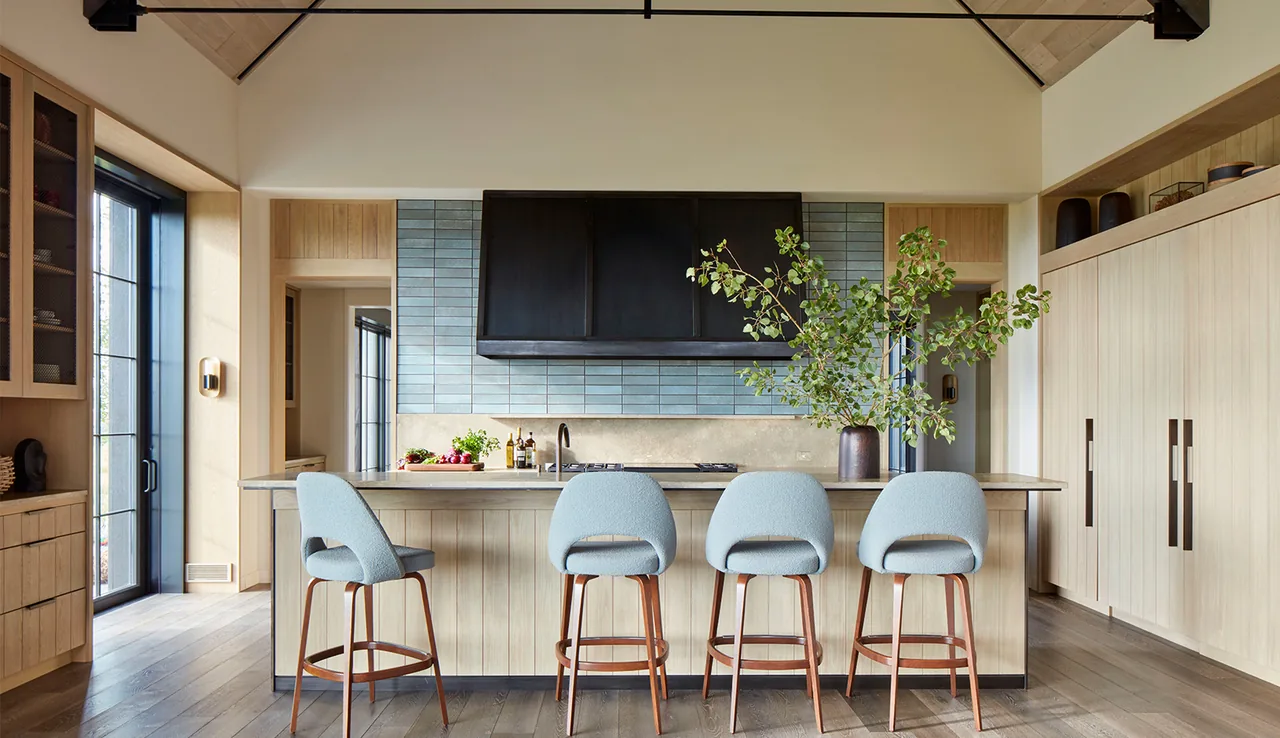 The kitchen in Western Retreat features a light wood island, blue tile backsplash, and black range hood under vaulted ceilings.