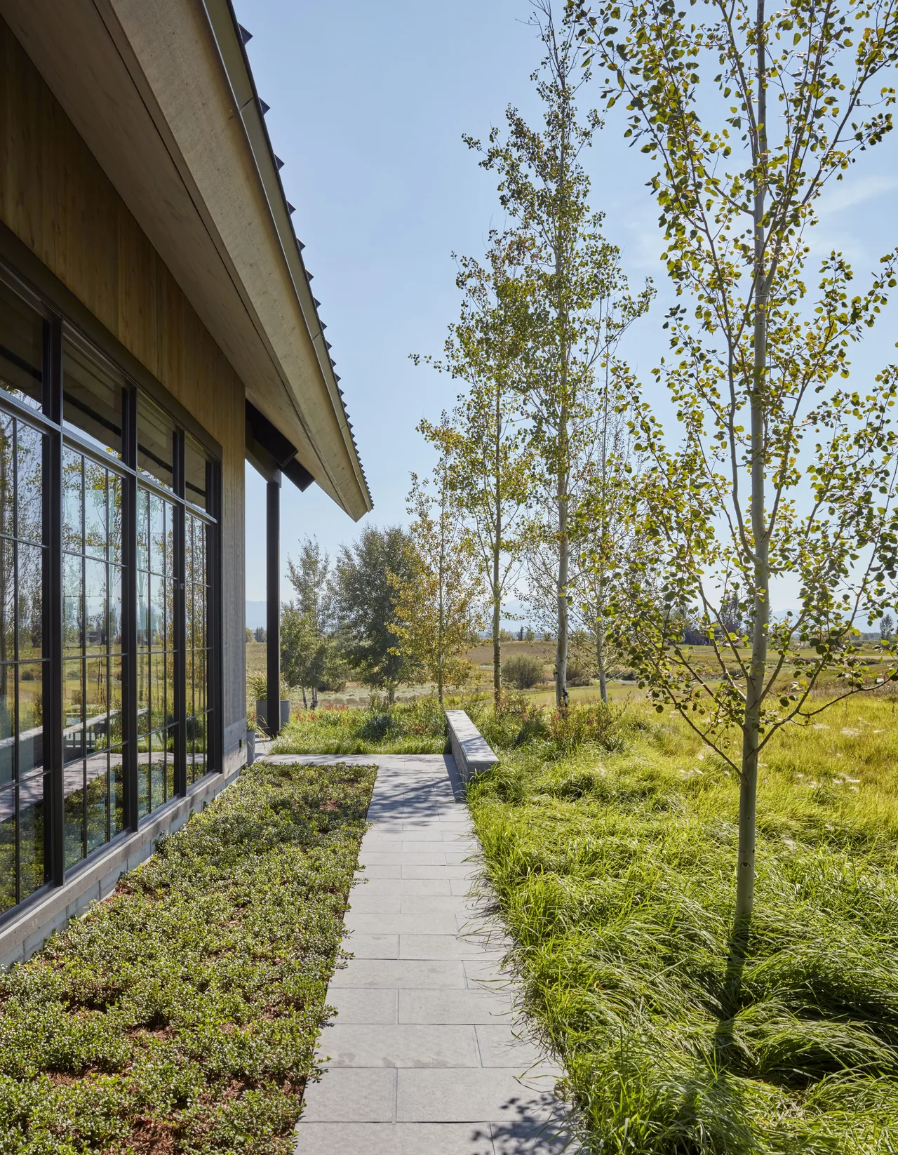 The Western Retreat features a wood siding exterior and grid-pattern windows overlooking a landscaped pathway and grassy field.