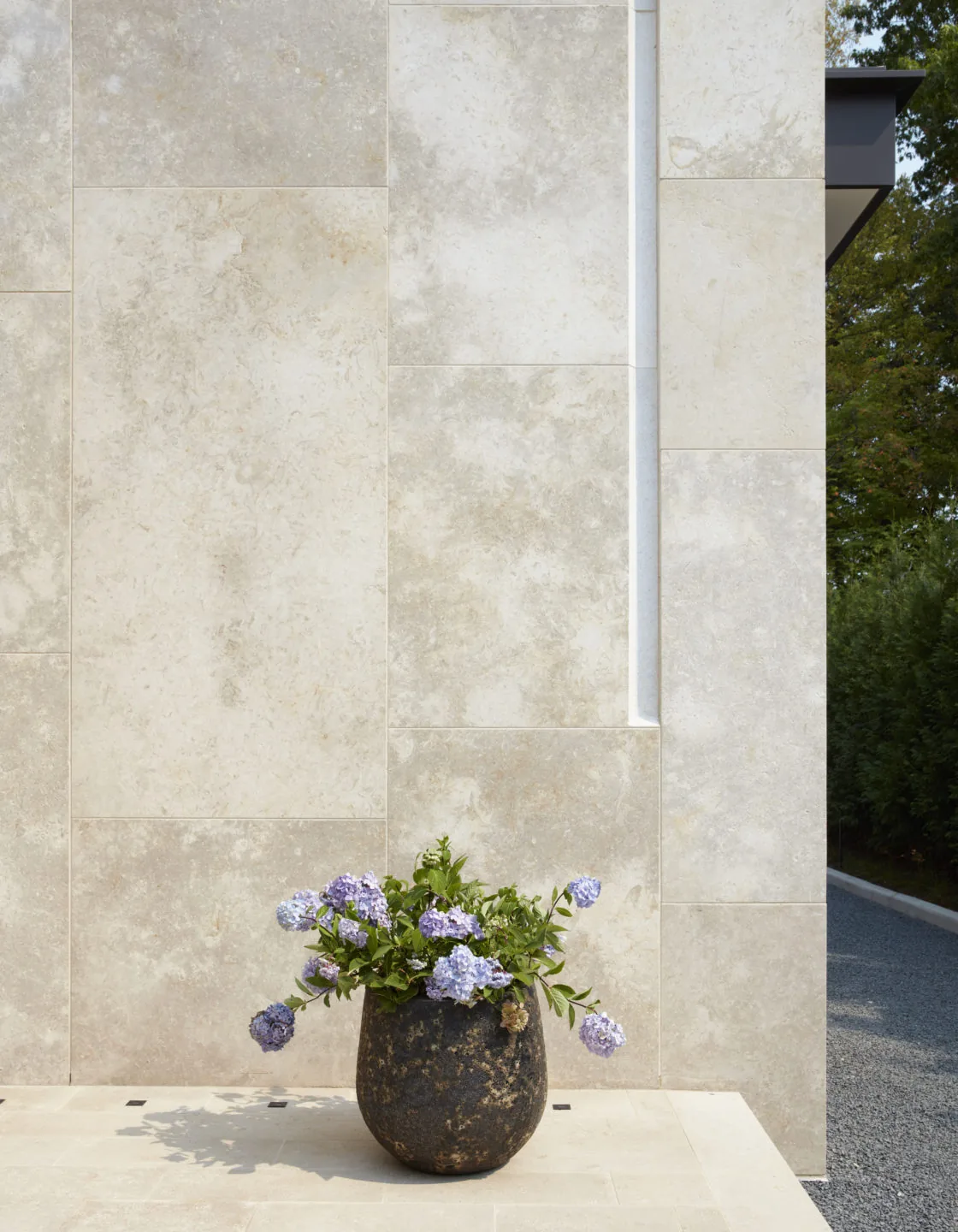 Stone planter with purple flowers arranged on a light stone patio by a beige stone wall.