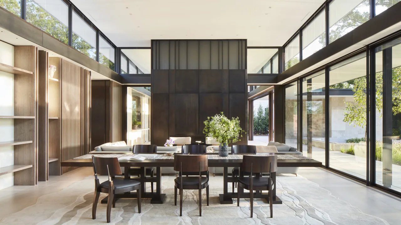 The Midwest Sanctuary dining room features floor-to-ceiling glazing and a dark paneled divider wall by Robbins Architecture.