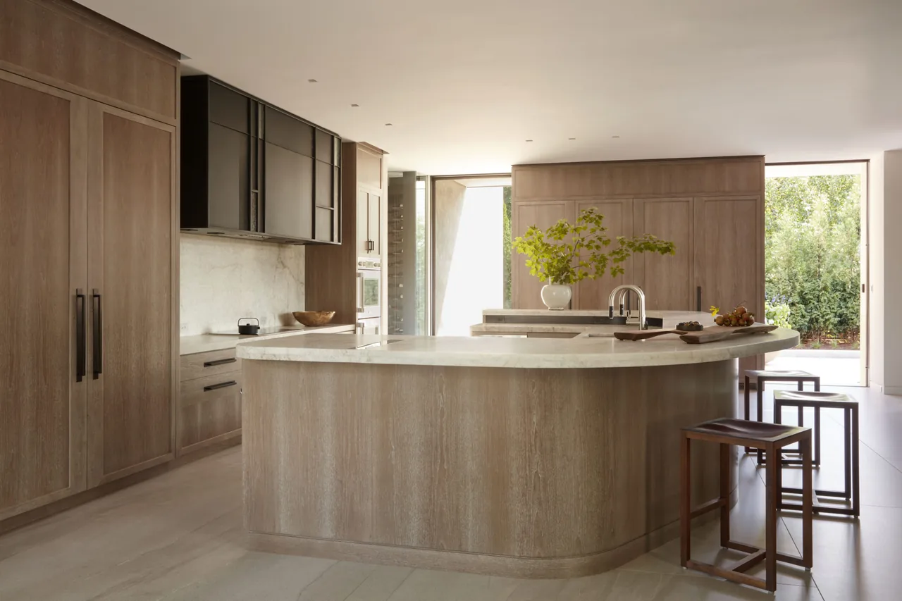 The Midwest Sanctuary kitchen features a curved island with stone countertops and wooden cabinets, designed by Robbins Architecture.