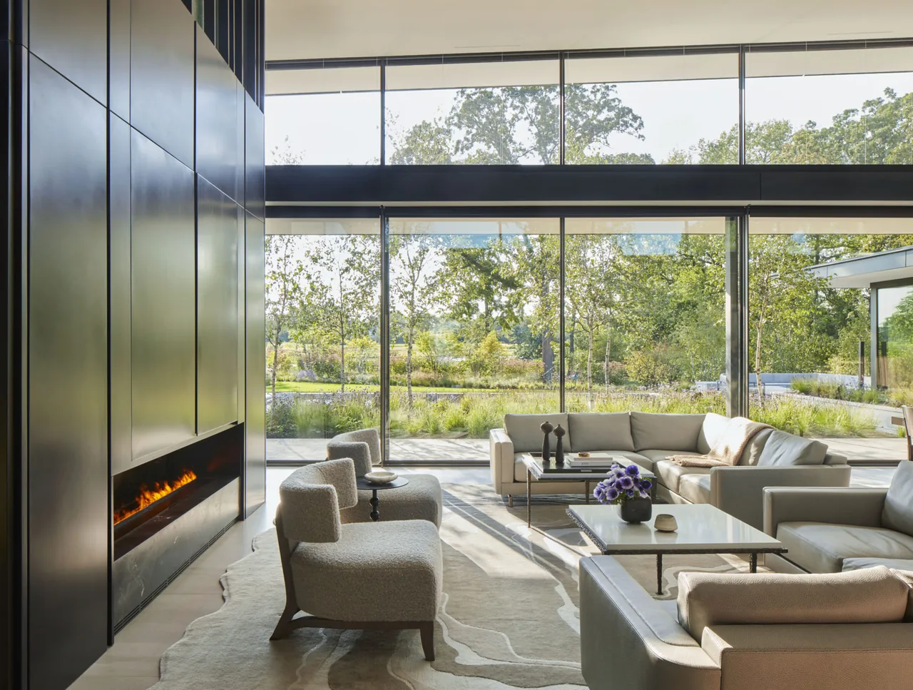 Living room features floor-to-ceiling windows, a linear fireplace, and modern furniture with a view of the outdoor greenery.