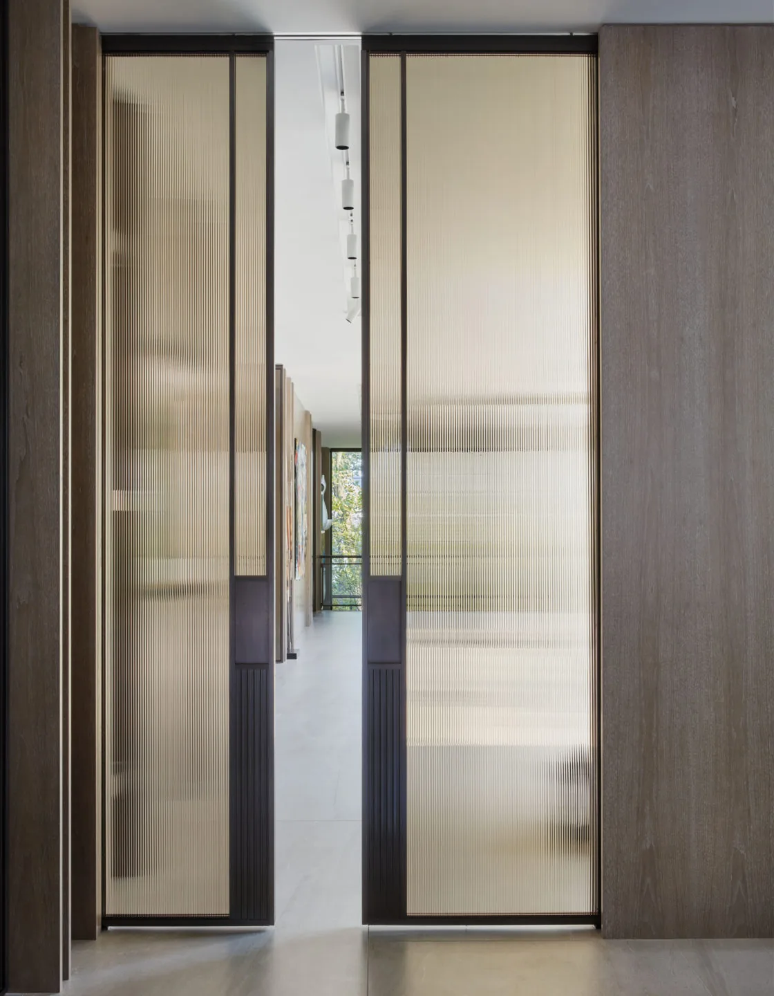 Corridor separated by translucent sliding panels featuring vertical fluted glass and wood panels.