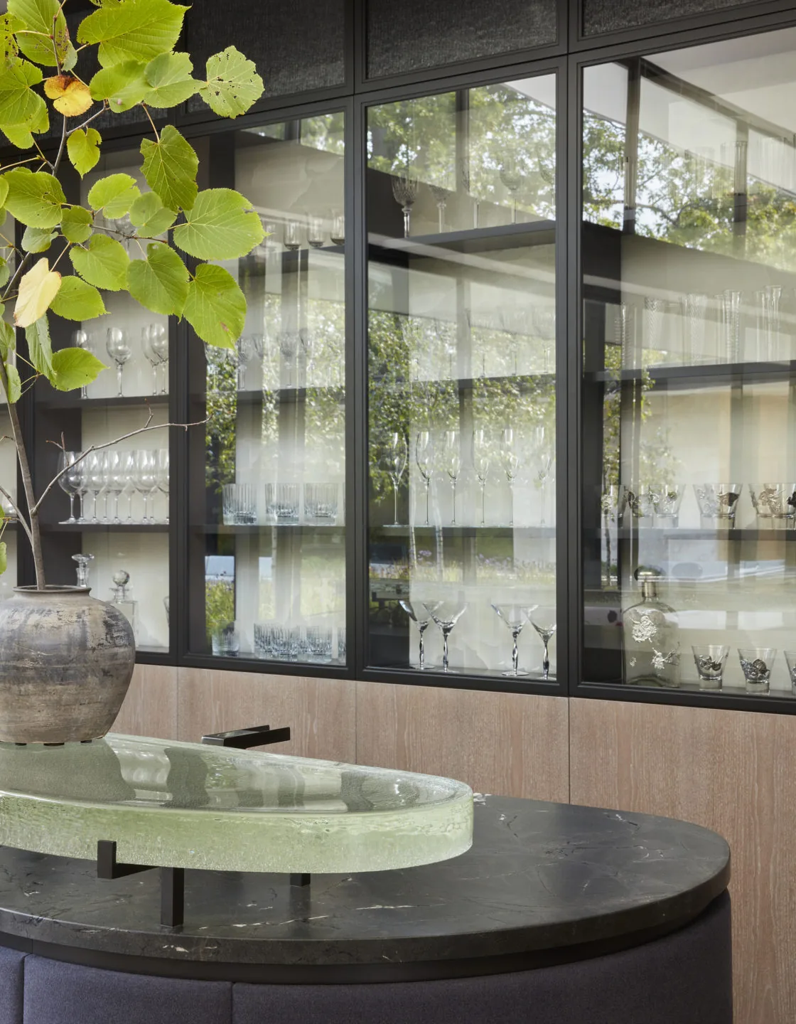 Glassware is displayed on shelves behind black framed glass cabinets above a wood-paneled wall.