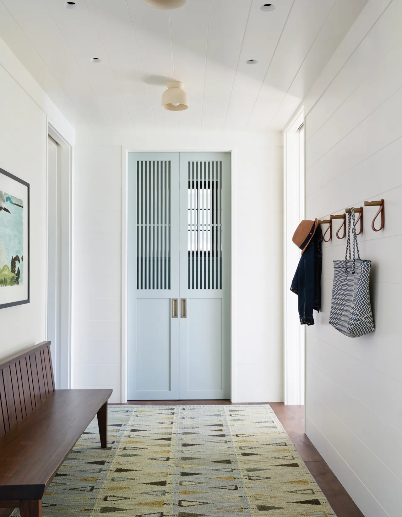 Entry hallway with blue double doors featuring vertical slats and a wooden bench along the left wall.