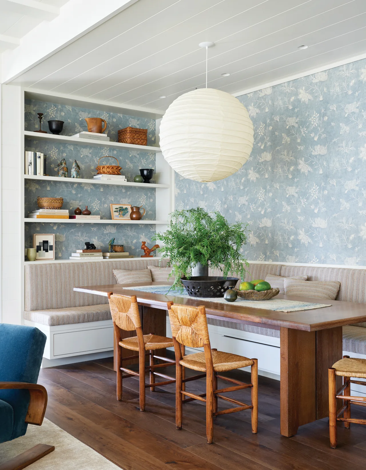 Dining nook with cushioned built-in benches, wooden dining table, and woven chairs under a large round pendant light.