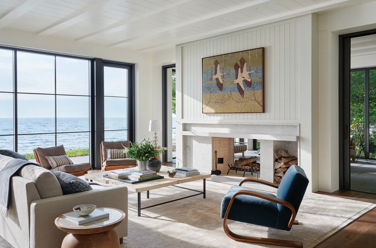 Living room in the Making Waves project by Robbins Architecture, featuring a stone fireplace and views of the water through large windows.