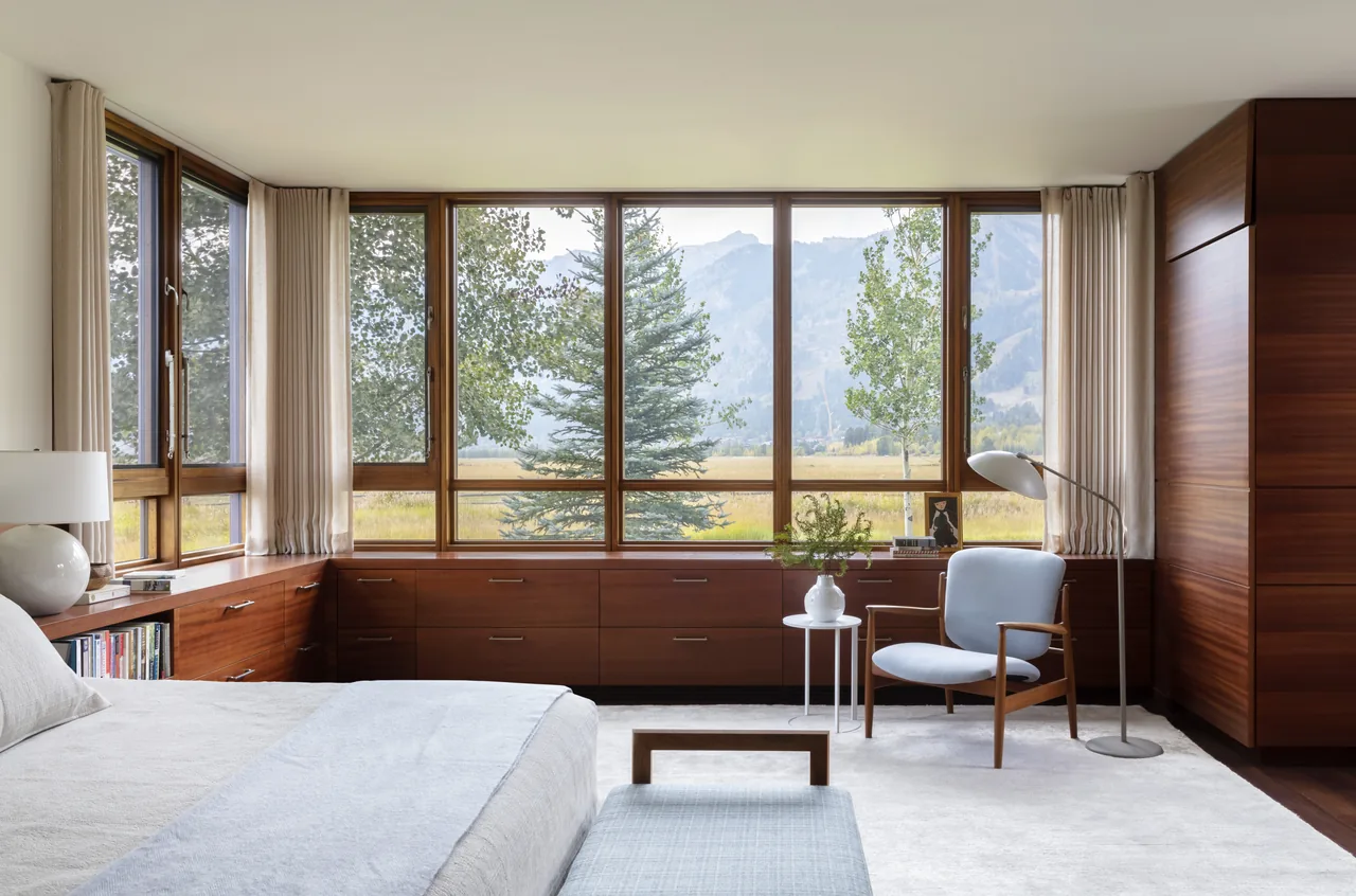 Bedroom features expansive wooden framed windows with a mountain view and wood-paneled cabinetry below.
