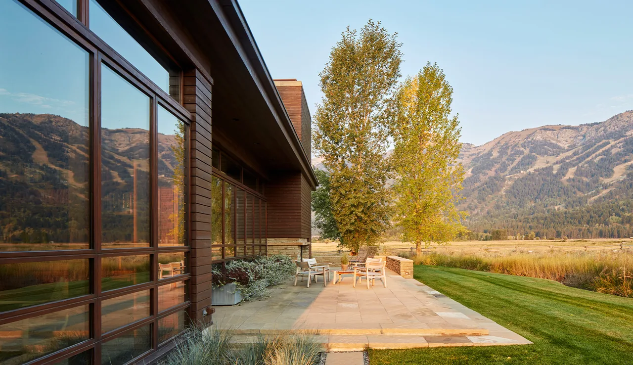 Patio next to the home with wood siding and large window walls reflecting mountain views.
