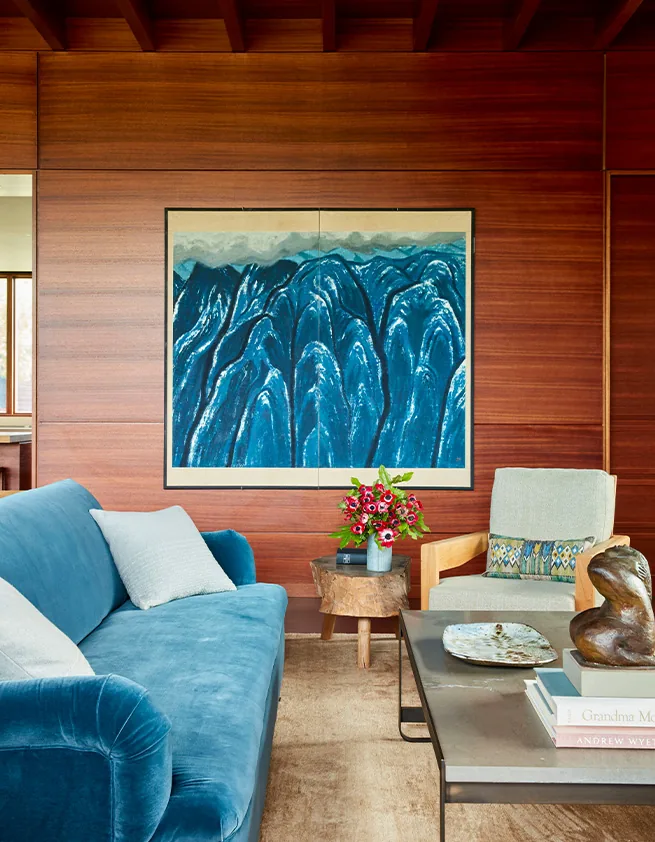 Living room features a blue velvet sofa, wooden paneled walls, and a painting of blue mountains.