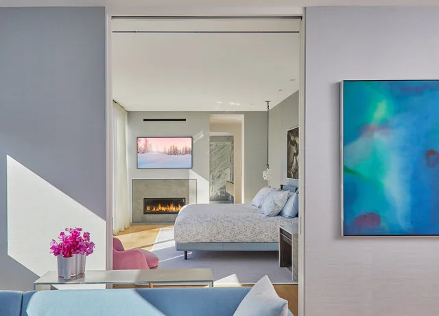 Bedroom with fireplace and visible bathroom seen from an adjacent living area with colorful artwork on the wall.