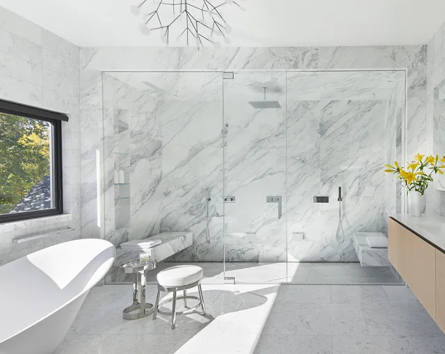 The Urban Woodland House bathroom features white marble surfaces, a freestanding tub, and a glass shower enclosure with modern fixtures.