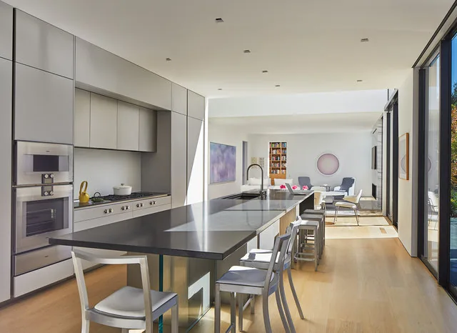 Open kitchen and living area with black kitchen island, white cabinetry, and sliding glass doors.