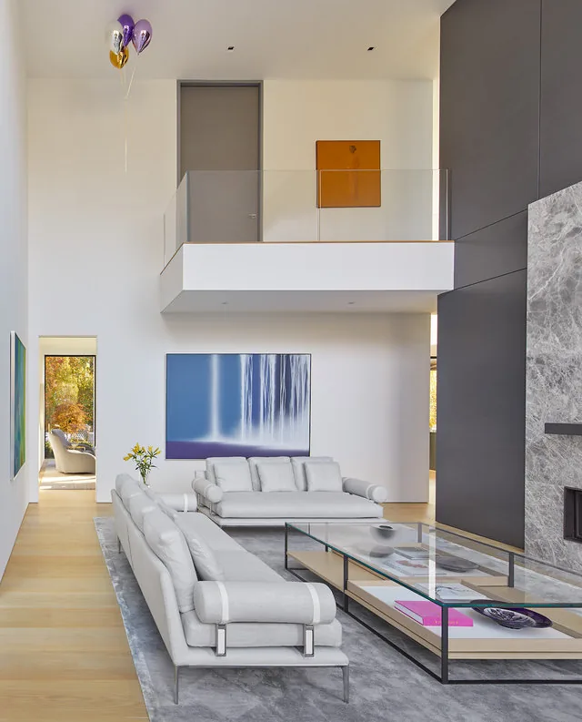 URBAN WOODLAND HOUSE living room features double-height ceiling, light furniture, and a glass balcony by Robert Gurney Architects.