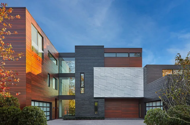 Urban Woodland House features a mixed facade of wood siding, dark stone, and light gray paneling by Robert Gurney Architects.